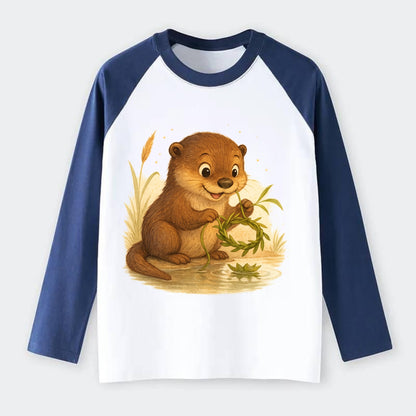 Otter weaving river reeds into a floating crown beside mirror-still - Raglan Long Sleeve T-Shirt - Blue