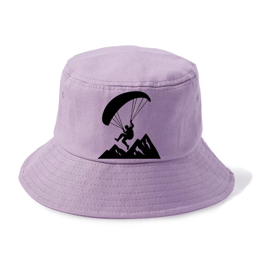 Paraglider soaring over mountain peaks - Bucket Hat