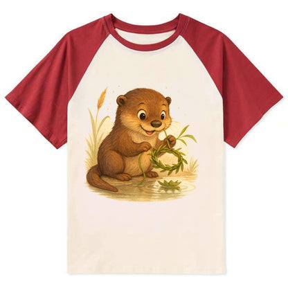 Otter weaving river reeds into a floating crown beside mirror-still water - Contrast Raglan T-shirt - Red